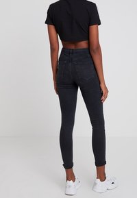 Černé skinny džíny s vysokým pasem vyrobené z denimové látky s hladkým povrchem, s dvěma zadními kapsami a úzkým otvorem nohavic.