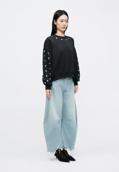 Čierna mikina s kovovými striebornými cvočkami na rukávoch, kombinovaná s oversize svetlomodrými rifľami s ošúchanými okrajmi. Nosené čierne topánky na podpätku.