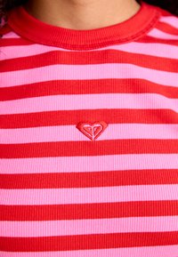 Top a righe rosse e rosa con coste, dotato di collo a giro e un piccolo logo a forma di cuore rosso ricamato sul lato sinistro.