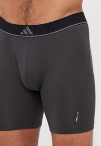 Čierne športové nohavičky s kontrastným textúrovaným pásom, s priliehavým strihom a malou značkou "AEROREADY" na dolnej časti nohy.