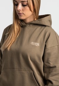 Khaki mikina s kapucňou vyrobená z jemného materiálu, s prednou kapsou a diskrétnym výšivkou loga značky na hrudi.