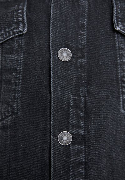 Black denim shirt featuring silver snap buttons, chest pockets, and visible stitching. Fabric has a textured surface with a slight sheen.