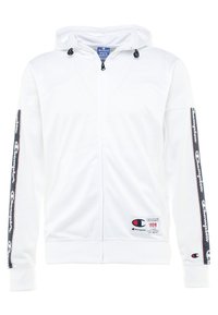 Vit zip-up hoodie i mjukt material, har huva med dragsko, logotypdetaljer på ärmarna och ett märke på den nedre framsidan.