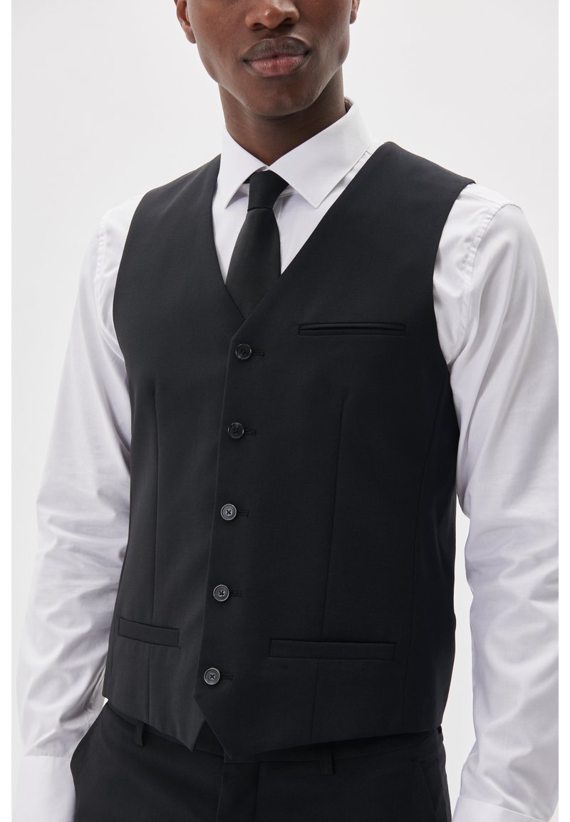 princess polly baby blue dress charming and red haired asian woman in white shirt, black tie, vest and  pants looking at camera on grey shaded background, business casual fashion,  ge Stock Photo