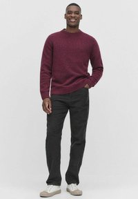 Bordeaux gebreide sweater met een ronde hals en geribbelde manchetten, gecombineerd met zwarte broek en witte sneakers met beige accenten.