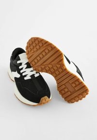 Baskets noir et blanc en matériaux mesh et daim, avec une semelle en gomme texturée et des lacets blancs contrastants.