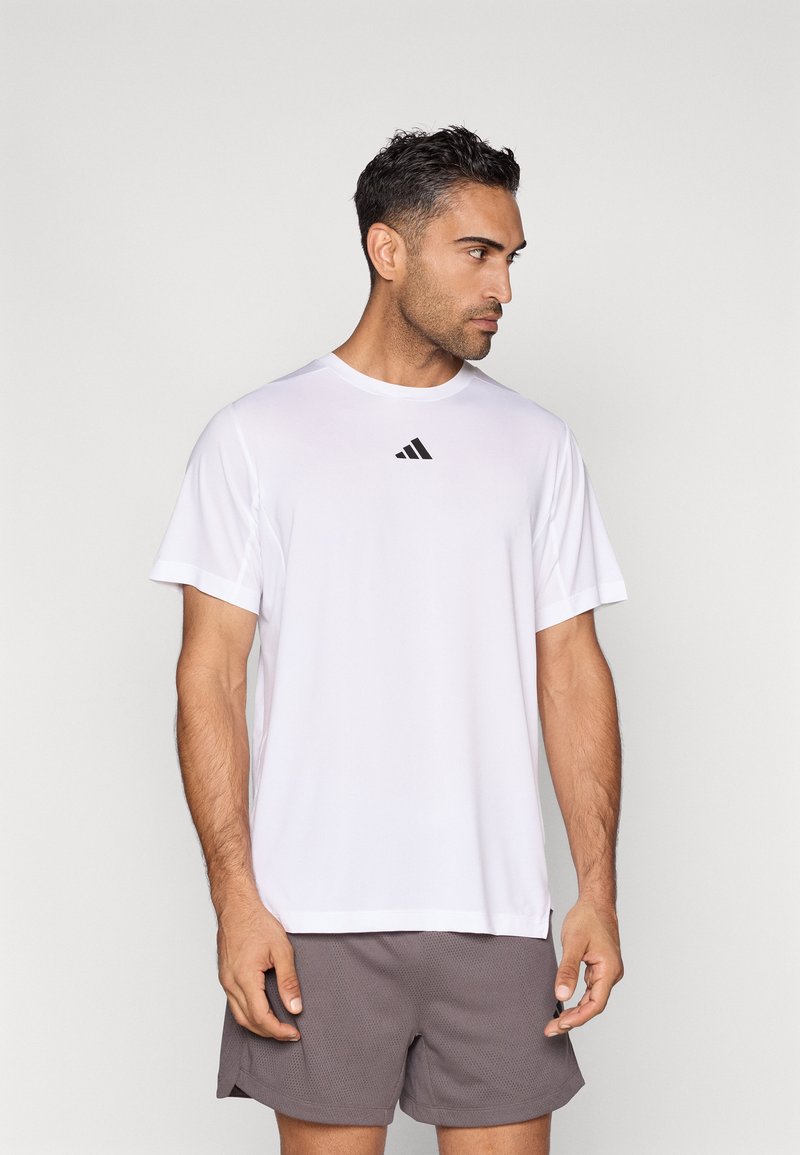 Hvid atletisk t-shirt lavet af åndbart stof, med rund hals og korte ærmer samt en lille sort logo på brystet.