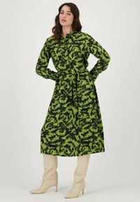 Groene en zwarte gestreepte jurk, lange mouwen, kraag, ceintuur om de taille, midi-lengte, gecombineerd met beige kniehoge laarzen.