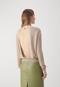 Pull en tricot beige avec dos ouvert, ourlet côtelé, manches longues. Associé à une jupe en cuir verte avec un détail de fente centrale.