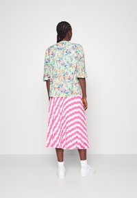 Top de mangas curtas com padrão floral em verde claro com toques de cor, combinado com uma saia plissada em rosa e branco listrada. Ténis brancos usados.