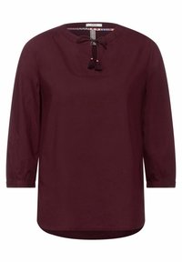 Blouse bordeaux à manches longues avec encolure ronde et détail de lien à pompons à l'avant, dotée de poignets froncés subtils.