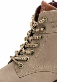 Botte beige en cuir à lacets avec des œillets métalliques, des lacets marron et beige à motifs, et un petit logo de marque embossé près de la cheville.
