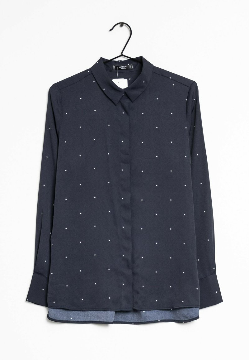Chemise bleu marine à manches longues avec petits pois blancs, boutonnée sur le devant et col pointu, suspendue sur un cintre noir sur fond blanc.