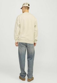 Sudadera beige de manga larga, con puños y dobladillo acanalados; combinada con jeans azul claro y calzado marrón; vista desde la parte posterior.
