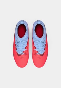 Scarpe da calcio Nike con una parte superiore rossa e azzurro chiaro, texture a righe, lacci sottili e un logo swoosh nero sul lato.