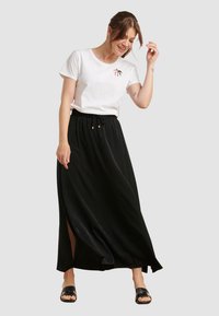 Witte katoenen t-shirt met een kleine kleurrijke palm graphic, gecombineerd met een zwarte maxi rok met een trekkoord in de taille en een zijsplit.