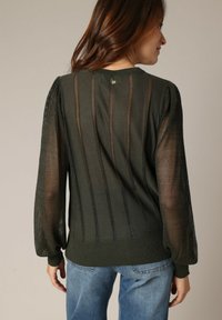 Donkergroen mesh trui met een geribbelde boord, pof mouwen en een verticale gestreepte patroon. Bevat een knoop bij de achterkant van de halslijn.