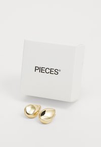 Zlatne suknje u obliku suze s glatkom, refleksivnom površinom, prikazane uz bijelu kutiju označenu s "PIECES."