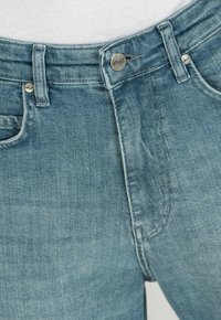 Jeans de mezclilla azul claro con corte recto, herrajes plateados, diseño de cinco bolsillos y una textura ligeramente desgastada en el frente.