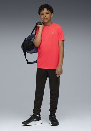 T-shirt de sport rouge, pantalon de survêtement noir et baskets noires. Sac bleu avec accents en maille. Manches courtes, design simple et silhouette ajustée.