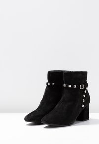 Stivali alla caviglia in suede nero con punta appuntita, tacco a blocco e una fascia decorativa con borchie argentate lungo il lato e attorno alla caviglia.
