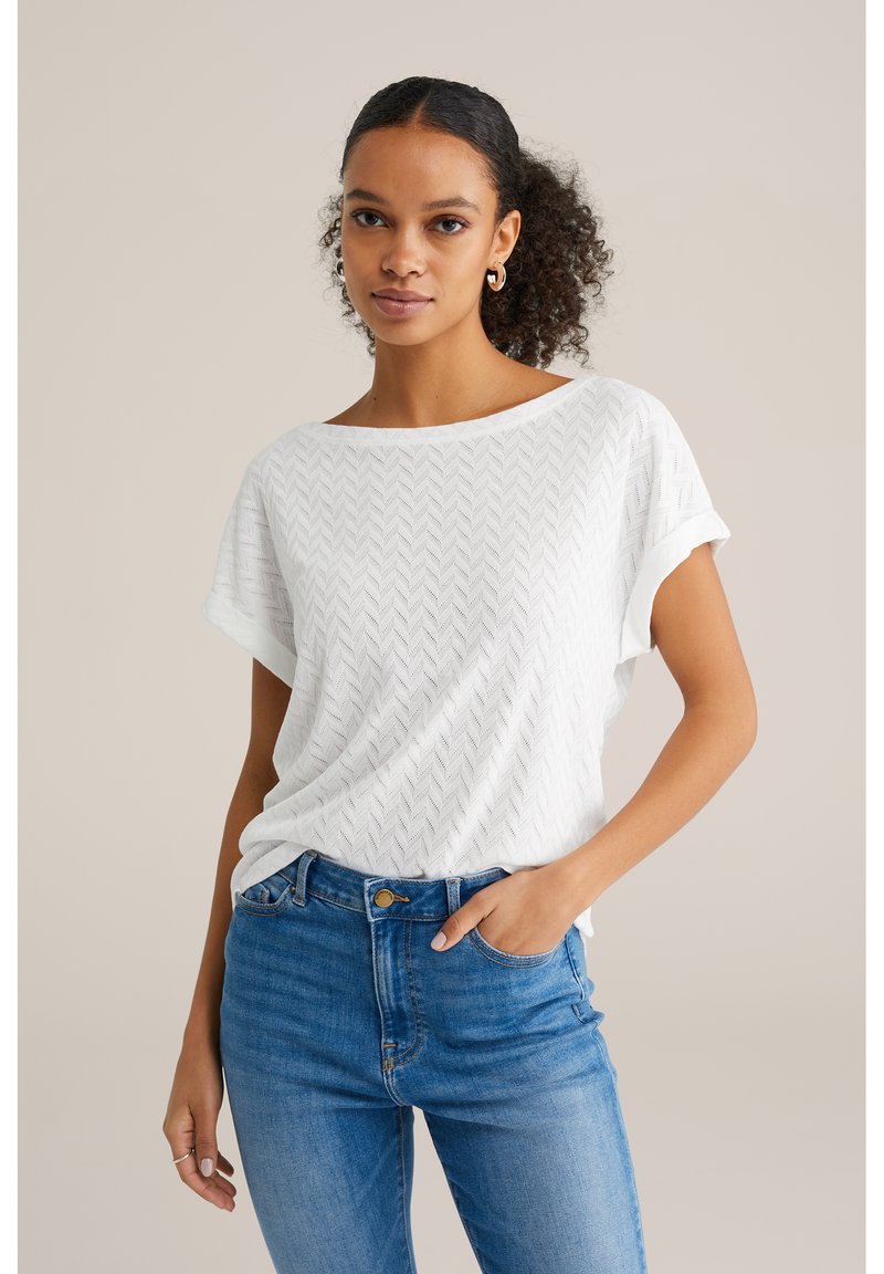 Top alb cu mânecă scurtă, cu un model texturat în zigzag, asortat cu blugi albastre cu talie înaltă. Mâneca are un design rulat.