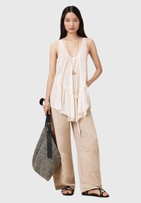 Lichtbeige mouwloze top met een peplumontwerp, gecombineerd met losse crème-kleurige broek en een gestreepte zwart-witte tas.