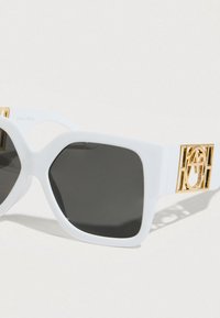 Λευκά υπερμεγέθη γυαλιά ηλίου με σκουρόχρωμους φακούς. Διαθέτουν χρυσαφί μεταλλικά στοιχεία στα πλαϊνά με γεωμετρικό σχέδιο κοπής.