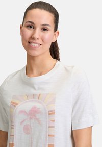 Witte t-shirt met korte mouwen met een centrale grafiek van een palmboom, zon en abstracte patronen in zachte roze en gele tinten.