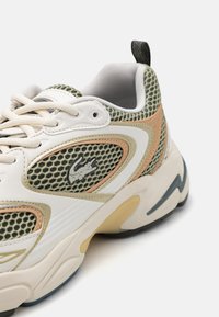 Lacoste sportcipők hálós felsőrésszel krém és zöld színben, bézs kiegészítőkkel és fekete logóval, masszív talppal és textúrás elemekkel tervezték.
