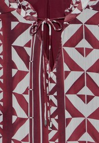 Tissu à motif géométrique bordeaux et blanc avec un col en V et un cordon de serrage noué avec des extrémités en métal argenté.