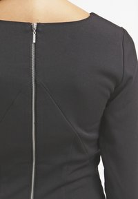 Black dress with a rounded neckline, featuring a visible silver zipper at the back and textured fabric with seam detailing.