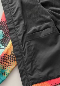 Veste colorée avec un tissu noir texturé d'un côté et une doublure vibrante à motifs dans des nuances de bleu, rose et orange.
