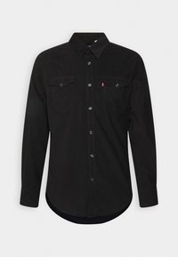 Chemise noire à manches longues avec deux poches poitrine, boutons pression et col pointu sur un fond clair uni.