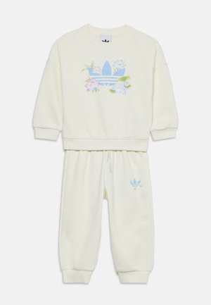 Set van crèmekleurige sweatshirt en broek met blauw Adidas trefoil-logo, versierd met pastelbloemmotieven op trui en broek.