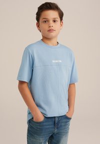 Jasnoniebieska koszulka z krótkim rękawem o okrągłym dekolcie, z poziomą szwem i nadrukiem "BLUE RIDGE DENIM" na przodzie.