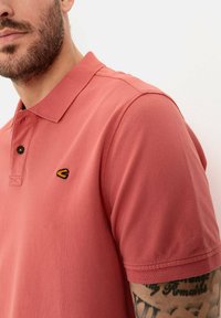 Polo shirt in zalmroze, gemaakt van textuurstof. Kenmerkt zich door een klassieke kraag, twee knopen en een klein zwart en geel logo op de borst.