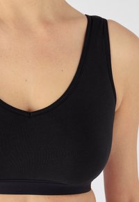 Zwarte bralette van een gladde, rekbare stof. Het heeft een ronde halslijn en brede schouderbanden, en biedt een simpel, naadloos ontwerp.