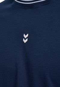 Mörkblå bomullströja med rund hals, prydd med vita horisontella ränder vid halsringningen och en vit chevron-logotyp på bröstet.