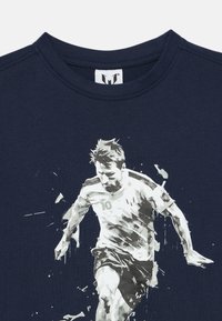 Μπλε βαθύ βαμβακερό T-shirt με λευκή γραφική εκτύπωση ενός ποδοσφαιριστή σε κίνηση, με λεπτομέρειες ψεκασμού και τον αριθμό "10" στην εμφάνιση.