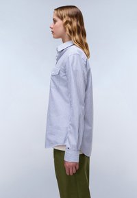 Striped long-sleeve shirt in light blue and white cotton with a button-down collar, two front pockets, and buttoned cuffs.