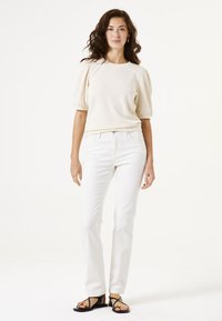 Haut à manches courtes crème avec manches bouffantes, associé à un jean blanc à jambe droite et des sandales noires à lanières. Tissu lisse, coupe décontractée.