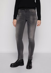Jeans skinny grises con una textura suave, cintura de altura media y un desvanecimiento sutil. Combinados con botas negras hasta el tobillo.