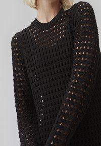 Maglione nero in maglia leggera con una trama in rete aperta, colletto rotondo e maniche lunghe con vestibilità ampia e dettagli a fantasia.