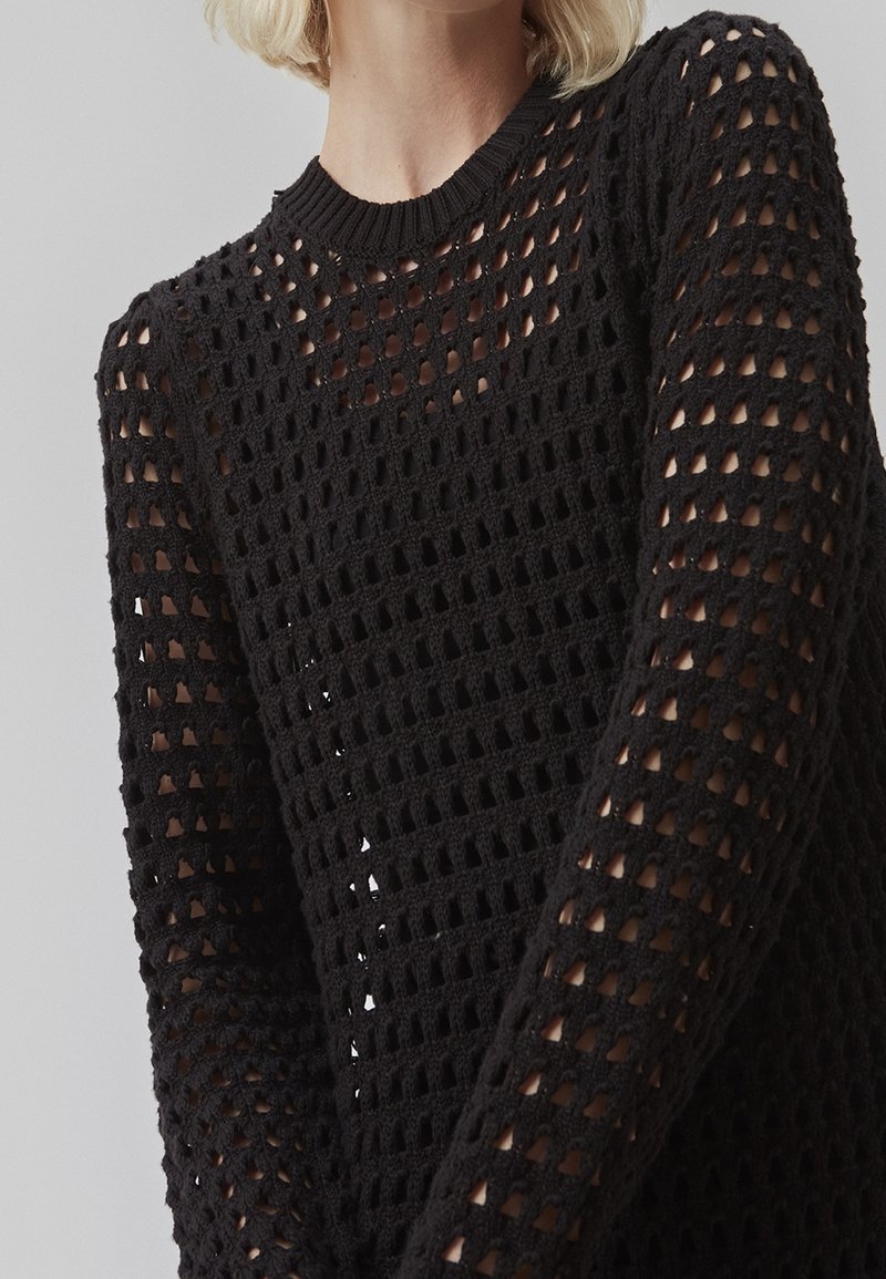 Maglione nero in maglia leggera con una trama in rete aperta, colletto rotondo e maniche lunghe con vestibilità ampia e dettagli a fantasia.
