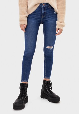 Mørkeblå slidte skinny jeans med rifter og høj talje, parret med sorte chunkykorte snørebåndsstøvler.