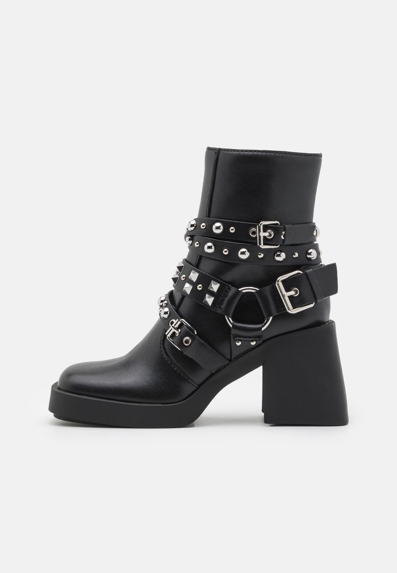 Bottine noire à talon épais, décorée de plusieurs brides en cuir cloutées et de boucles argentées sur un fond uni.