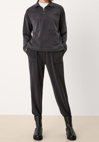 Felpa zip grigia scura con due tasche anteriori, abbinata a pantaloni a gamba affusolata con orli elasticizzati e una texture liscia. Stivali neri alla caviglia.