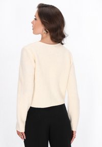 Maglione lavorato a maglia color crema con un motivo testurizzato, maniche lunghe e un design corto, con sottili riflessi argentati sparsi.