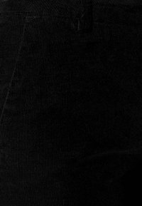 Tissu en velours côtelé noir présentant des nervures verticales et une texture lisse, offrant une vue rapprochée du matériau et des détails de design.